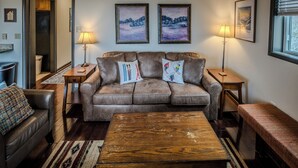 A cozy living room with a brown leather sofa, two framed landscape paintings, and a wooden coffee table.