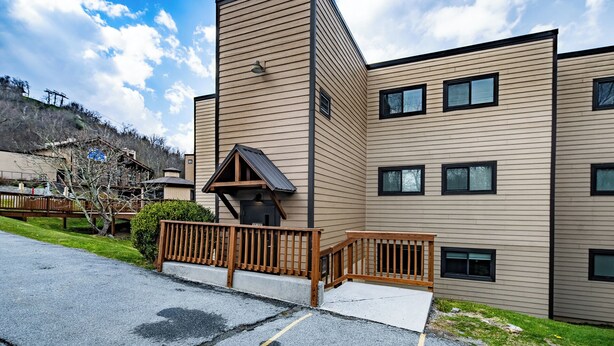 A modern multi-story building with a flat roof, a small porch with a railing, and a paved driveway.
