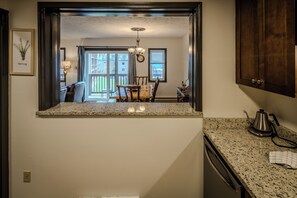 A kitchen with a granite countertop, a coffee maker, and a view into a dining area with a table and chairs.