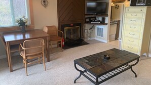Una sala de estar acogedora con chimenea, un comedor con mesa y sillas de madera, un televisor y una cocina con armarios y electrodomésticos.