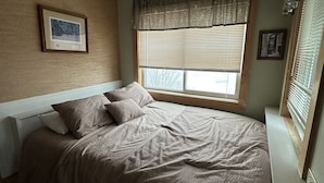 Un dormitorio con cama, ventana con persianas y un cuadro en la pared.
