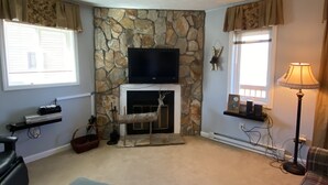 A living room with a stone fireplace, a flat-screen TV, a sofa, and a lamp. - Sugar Ski Comfort Two Bedroom - Unit 631 (Sugar Mountain)