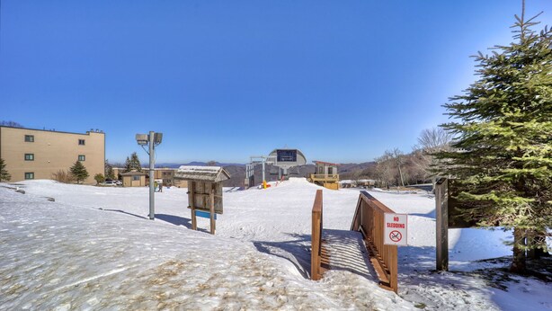 A snowy outdoor area with a wooden fence, a 'No Sledding' sign, and a building in the background. - Sugar Ski Comfort Two Bedroom - Unit 631 (Sugar Mountain)