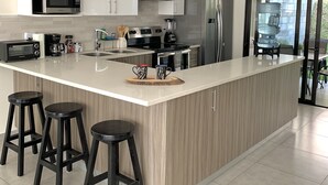Una cocina moderna con armarios blancos, un refrigerador de acero inoxidable, un horno empotrado y una isla grande con taburetes de bar.