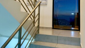 Una escalera con barandillas de metal y una baranda de vidrio a la izquierda, que conduce a una plataforma con vistas a un paisaje urbano nocturno.