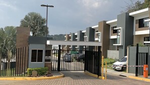Una entrada cerrada a un complejo residencial con arquitectura moderna, un camino pavimentado y un cielo despejado.