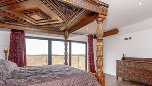 Une chambre à coucher avec un lit à baldaquin, une commode en bois et une grande fenêtre donnant sur un beau paysage.