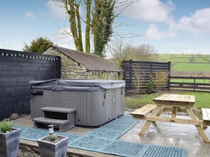 A hot tub with steps and a wooden table in a backyard with a stone wall, wooden fence, and trees.