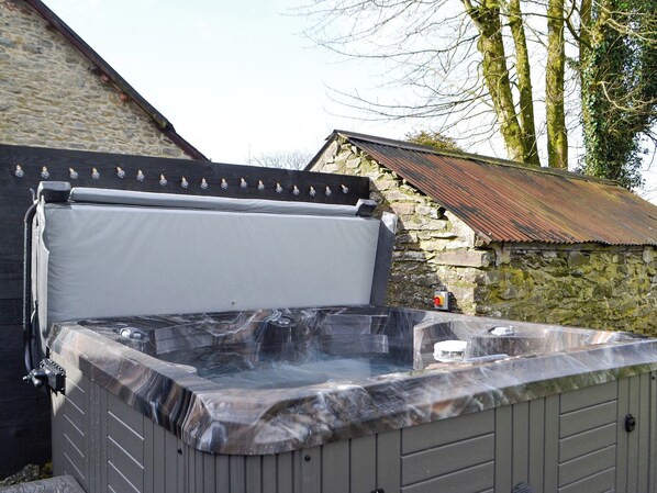 A hot tub with a stone wall backdrop, a wooden deck, and a rustic metal roof.
