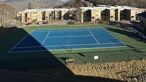 A tennis court surrounded by buildings with a clear sky.