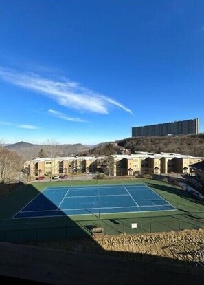 A tennis court surrounded by buildings with a clear sky.