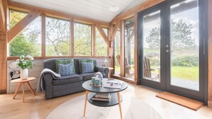 Una habitación acogedora con un sofá gris, una mesa de centro redonda y un amplio ventanal con vistas al exterior.