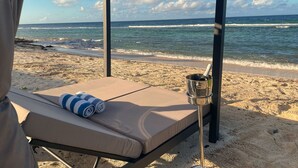 A beachside cabana with a single bed, a metal bucket, and a view of the ocean.