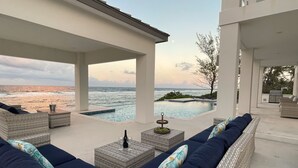 A modern outdoor lounge area with a pool, seating, and a view of the ocean.