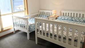 Una habitación con dos cunas blancas, cada una con una colcha estampada y una mesita de noche con lámpara.
