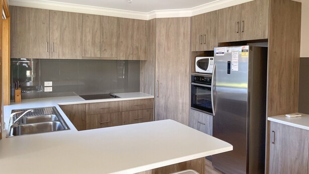Una cocina moderna con armarios de madera, electrodomésticos de acero inoxidable y encimera blanca.