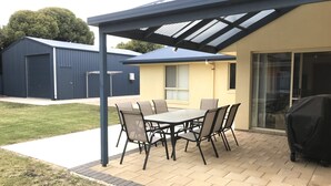 Un patio al aire libre con mesa y sillas, una zona cubierta y un edificio al fondo.
