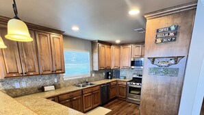 Una cocina con encimeras de granito, armarios de madera, refrigerador de acero inoxidable y una estación para café.