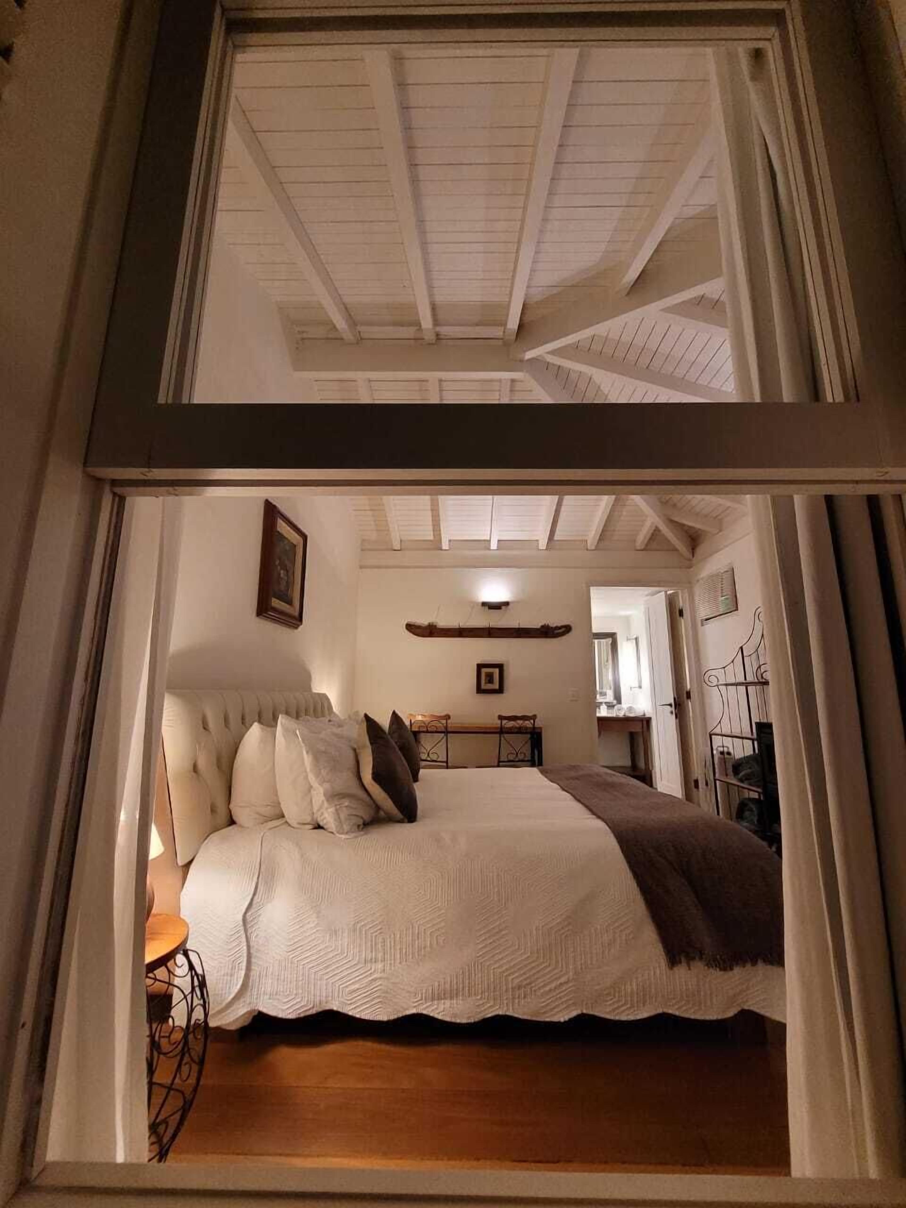 Ein Schlafzimmer mit einem Bett, einem Nachttisch, einem Sessel, einem Schreibtisch und einem Spiegel.