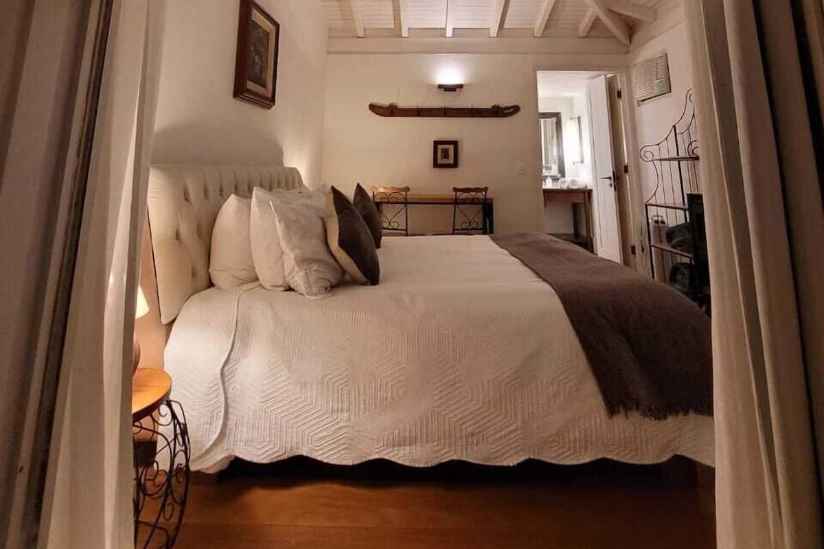 Ein Schlafzimmer mit einem Bett, einem Nachttisch, einem Sessel, einem Schreibtisch und einem Spiegel.