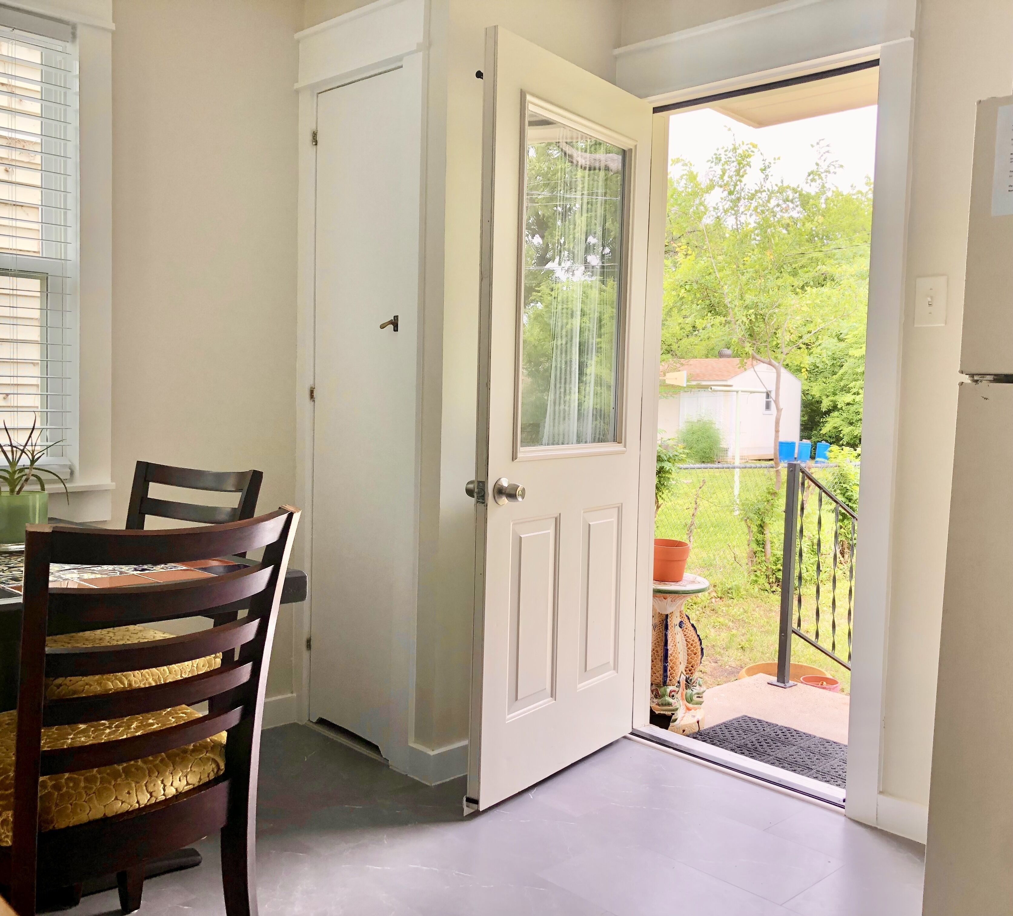 A room with a dining table, chairs, a white door, and a view of the outside.