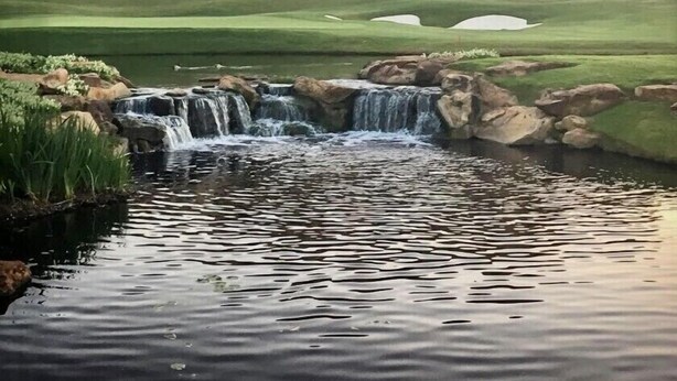 A hotel with a pool, a waterfall, and a golf course in the background.