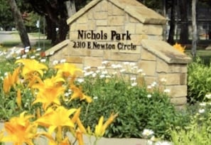 A stone sign with the text "Nichols Park 2310 E Newton Circle" surrounded by flowers.