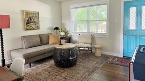 A living room with a sofa, a round coffee table, a chair, a decorative rug, a painting, and a blue door.