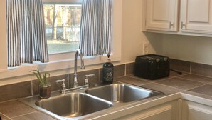 A kitchen with a double sink, a window with striped curtains, and a toaster on the counter.