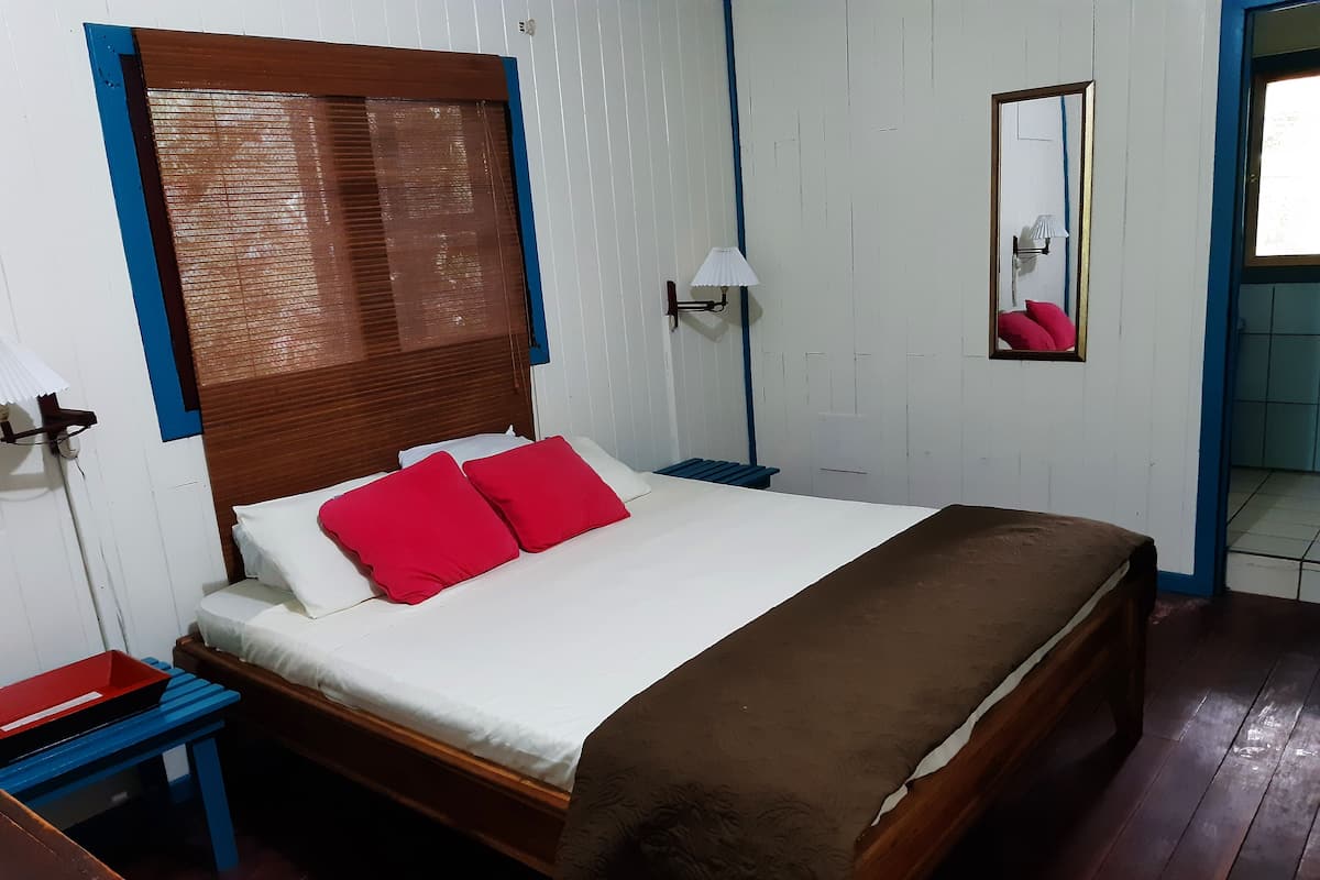 Una cama con cabecera de madera, dos almohadas rojas, colchón blanco y manta marrón.