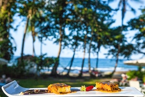 A dessert plate with two pieces of cake on a white plate, set against a backdrop of a beach and palm trees. - Lapalapa Beachfront (Cahuita)