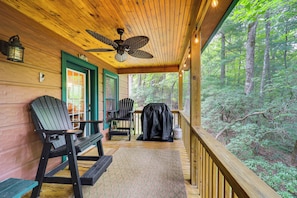 Enjoy a peaceful retreat on the porch with a forest view, featuring a ceiling fan, bench, and grill.