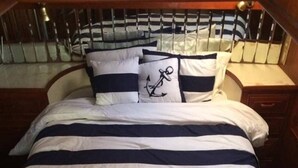 Een bed met marineblauwe en witte strepen, twee kussens met ankerprint en een houten hoofdbord.