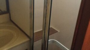 Een badkamer met een glazen douchecabine, een houten wastafelmeubel en een betegelde vloer.