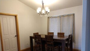 Un coin repas avec une table et des chaises en bois, un lustre et une porte avec un rideau.