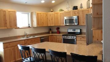 A modern kitchen with wooden cabinets, a central island with bar stools, stainless steel appliances, and a window providing natural light.