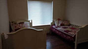 A small, well-lit room with two single beds, a window with blinds, and a radiator.