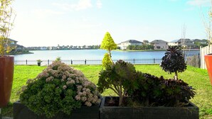 Um jardim com paisagismo, diversas plantas e vista para um lago e casas ao fundo.