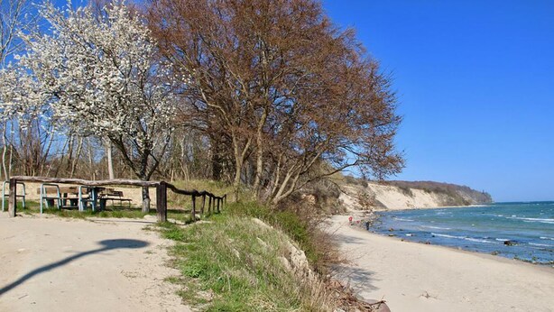 Een kustpad met een houten bankje, een zandstrand en uitzicht op zee.