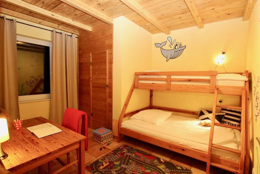A cozy room with a bunk bed, a wooden desk, a chair, a small rug, and a window with curtains.