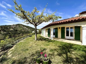 Experience a serene Mediterranean-style residence with a lush garden, tree, and paved driveway.