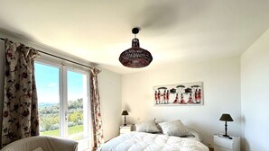 Un dormitorio con una cama, una silla, una mesita de noche, una lámpara y un cuadro en la pared.