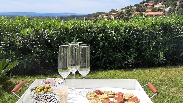 Un montaje para picnic con una bandeja de comida y bebidas sobre césped, con vistas a una ladera pintoresca.
