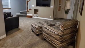 Un salon comprenant un canapé d’angle, un téléviseur fixé au mur et un escalier menant à un niveau supérieur.