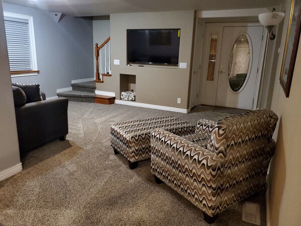 A living room with a sectional sofa, a television mounted on the wall, and a staircase leading to an upper level. - Farm House by River with trailer/RV parking(Pet Friendly including horses) (Brighton)