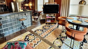 Een ruime woonkamer met een hoge plafond, een keukenhoek, een eettafel met stoelen en een televisie.