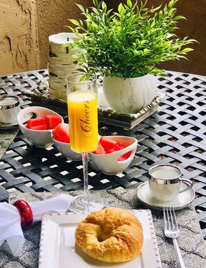 Ein gedeckter Tisch mit einem Glas Orangensaft, Wassermelonen in Schalen, einem Croissant und einer kleinen Topfpflanze.