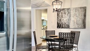 Una cucina moderna con un frigorifero in acciaio inossidabile, un'area pranzo con un tavolo rotondo e sedie in vimini, e un grande quadro astratto appeso al muro.