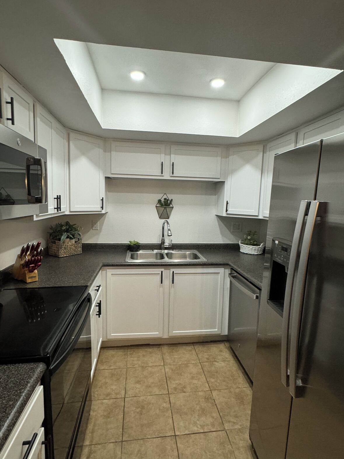 A modern kitchen with white cabinets, a stainless steel refrigerator, and a skylight.