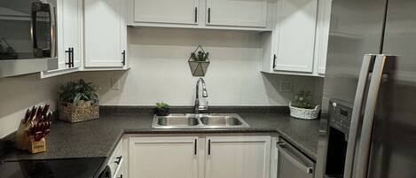 A modern kitchen with white cabinets, a stainless steel refrigerator, and a skylight.